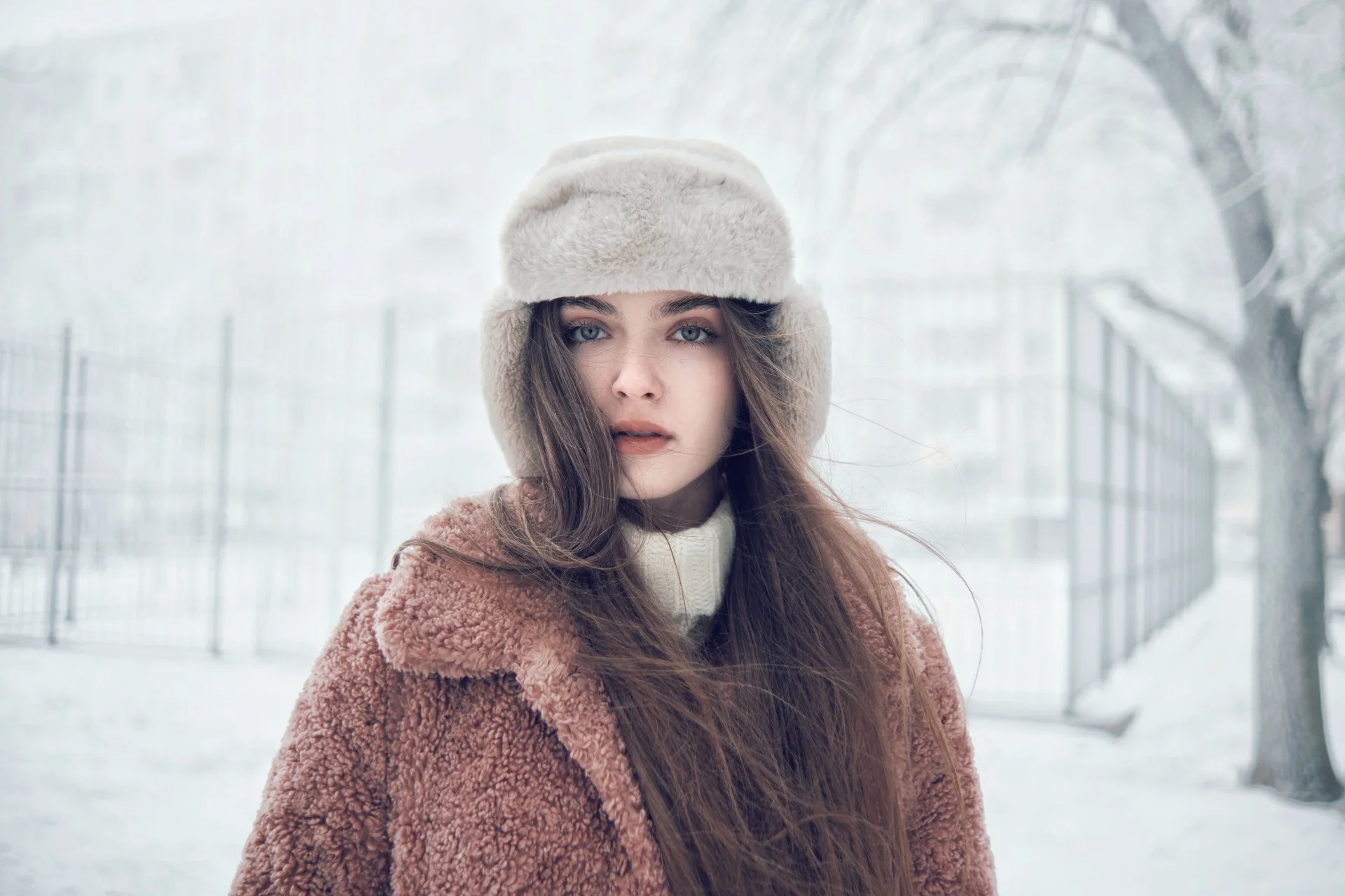 Portret stylowej kobiety w futrzanej czapce i płaszczu, stojącej na zaśnieżonym dworze.